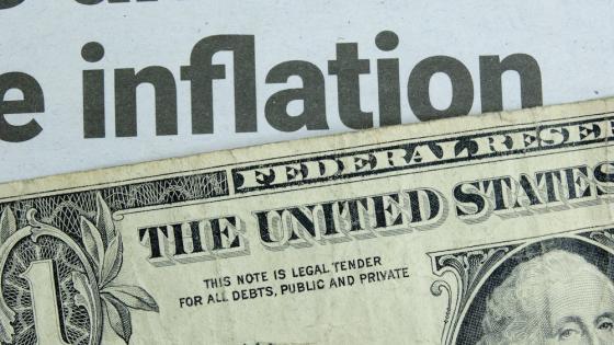 一张一美元的钞票躺在一张关于通货膨胀的报纸标题下面。