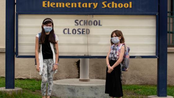 两名戴着面具的女学生在学校关闭的标志前